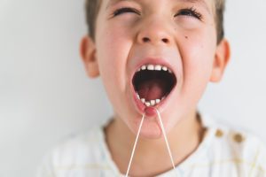 Cute boy pulling loose tooth using a dental floss. Process of removing a baby tooth.