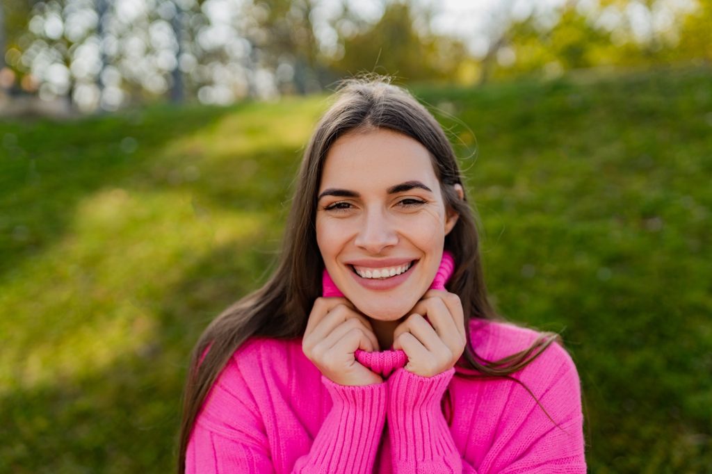 young smiling woman in pink sweater walking in green park