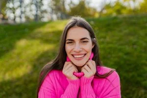 young smiling woman in pink sweater walking in green park