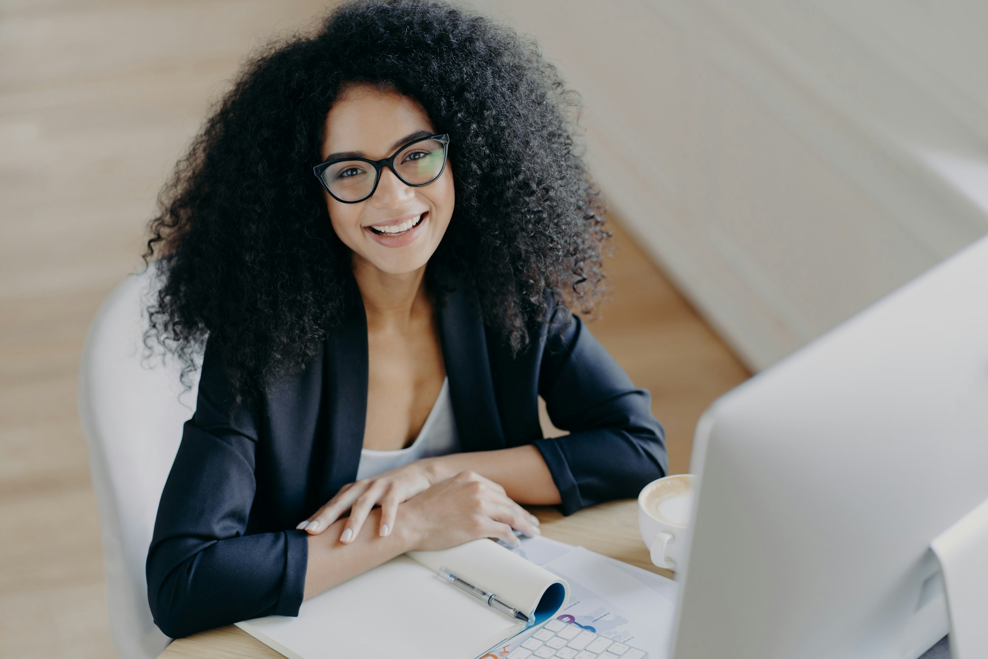 Glad African American businesswoman smiles pleasantly, notes information, makes notes